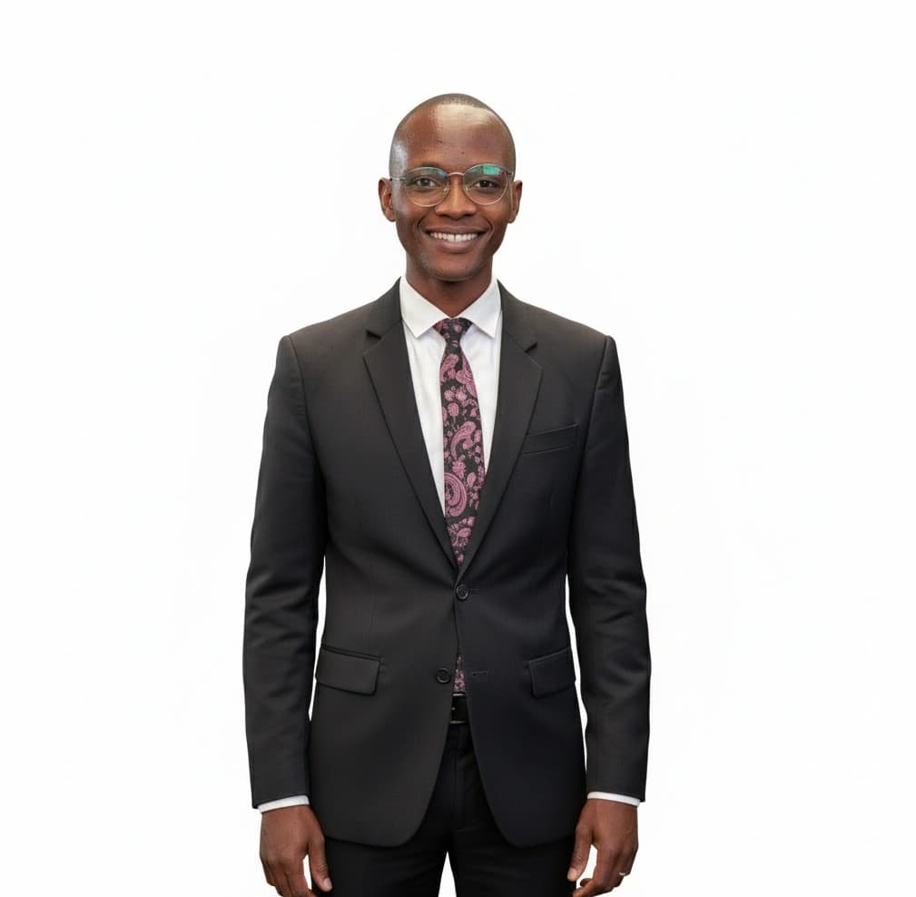 Homem negro sorridente usando óculos, terno preto, camisa branca e gravata estampada em fundo branco.